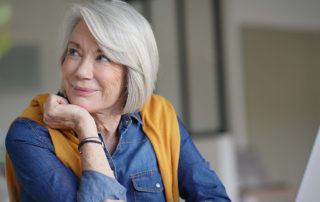 Beautiful senior woman looking pensive at home with laptop